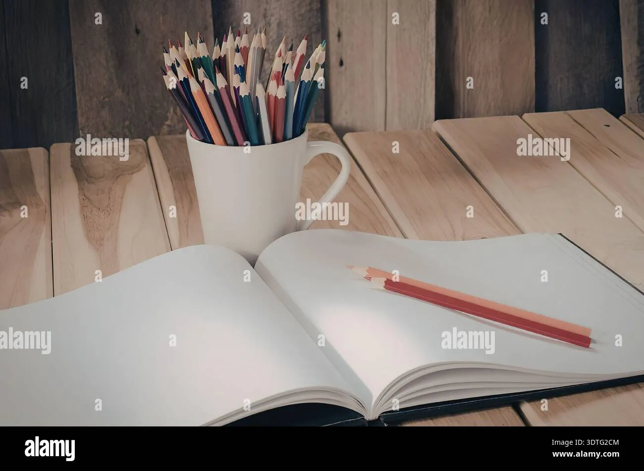an-open-book-with-a-red-pencil-on-it-and-a-mug-filled-with-colored-pencils-on-a-wooden-table-3dtg2cm Tạo thói quen tô màu trước khi đi ngủ giúp cải thiện chất lượng giấc ngủ rõ rệt